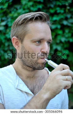 Man smoking an electronic cigarette outdoor. Profile.