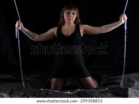 Photo of woman on knees holding chains on black background