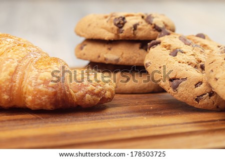 Chocolate chip cookies on a wooden board with a croissant