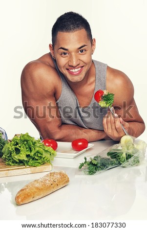 Portrait of muscle man eating vegetables on kitchen