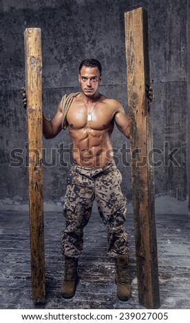 strong athletic man with naked body in military pants with wooden beams and rope on concrete wall
