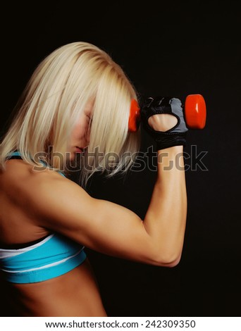 Good-shaped athletic girl covers her face with blonde hairs and holds dumbbell