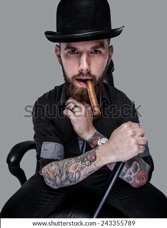 Tattoed male sitting on leather chair with cane in his hand