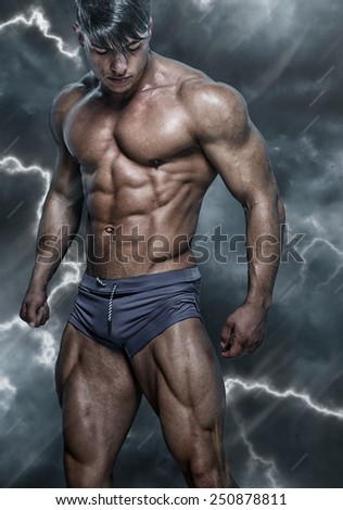 Portraite of handsome, muscular, sexy man in grey swimming trunks on fusion-gray background.