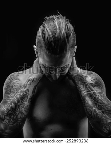 B/W portraite of a man with naked torso and tattooes. Isolated on black.