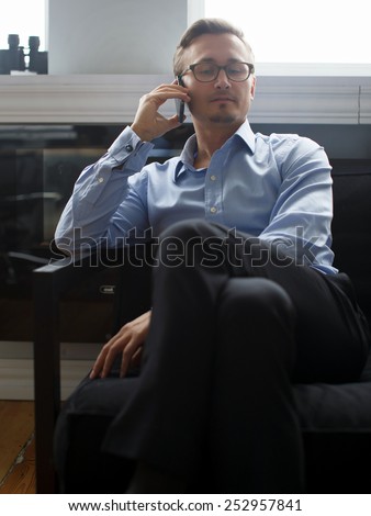 Young business man in dark blue suit pants and in a blue shirt colling with mobile phone in office.