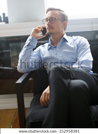 Young business man in dark blue suit pants and in a blue shirt colling with mobile phone in office.