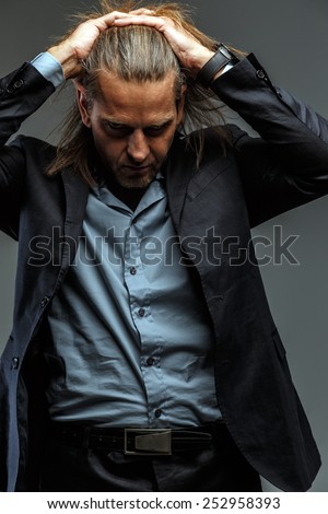 Portrait of handsome long-haired stylish man in dark grey suit. Isolated on gray background.