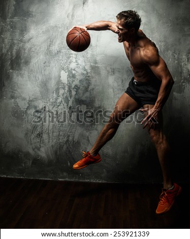 Awesome muscular male in a jump with basket ball in a hand. Grey background.