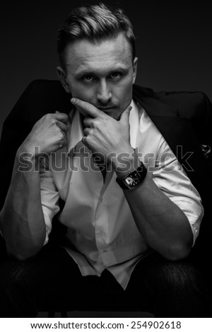 Black and white portrait of young business man in a suit on dark black background.
