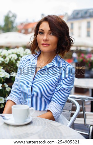 Woman in blue blouse sitting in street cafe.