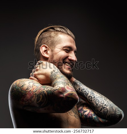 Portrait of a man with naked torso and tattooes. Dark and deep shadows.