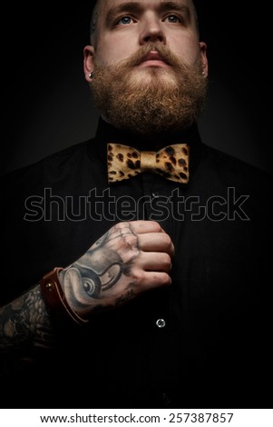 Portrait of the man with beard in black shirt and leopard bow tie. Isolated on dark gray background