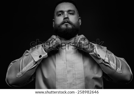 Black and white portrait of a man with beard and tattoos in white shirt and bow tie.