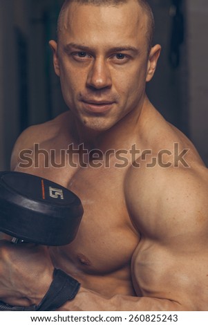 Strong muscular man bodybuilder shows his muscles holding dumbbell