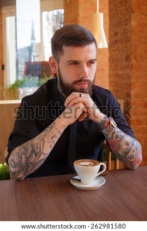 male with tattoos sitting at the table in a cafe.