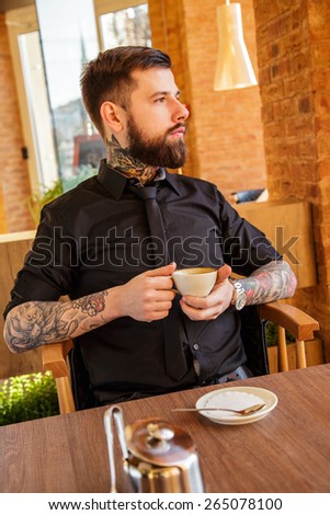 Guy with tattoos sitting at the table in a cafe.