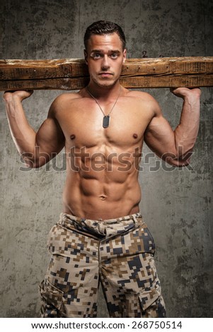 Man in army pants with naked torso holding board on his shoulders