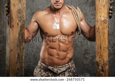 Muscular male body between two boards with rope on shoulder