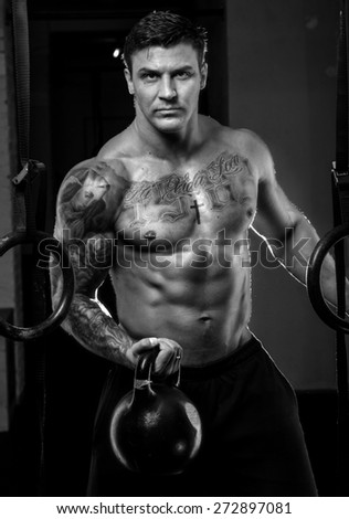 Muscular man with tattos doing exercises in a gym. Black and white photo
