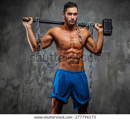 Shirtless muscular guy in blue shorts holding hummer on his shoulders. Grey background