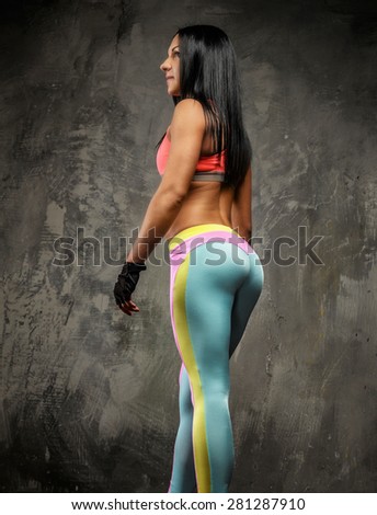 Slim fitness woman with long black hair in colorful sportswear on grey background