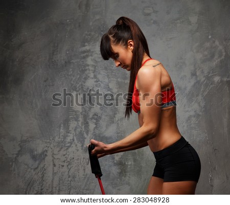 Fitness woman in sportswear doing exercises with expander on grey background. Side view