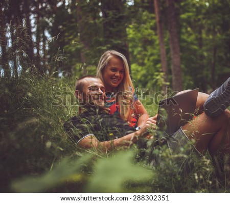 Man and woman with laptop lying on grass in the forest.