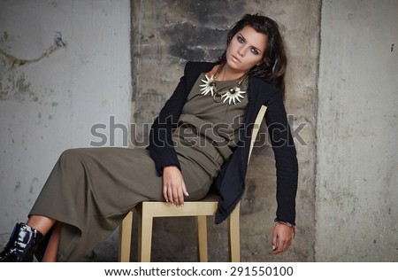 Woman with long black hair in dark green dress posing on chair.
