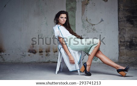 Attractive woman with long dark hair in white dress posing on chair in repair room.