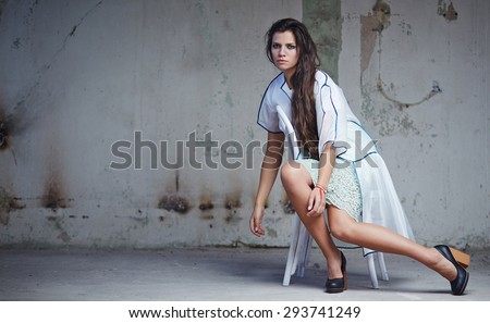 Attractive woman with long dark hair in white dress posing on chair in repair room.