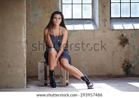 Slim female with long brown hair in sexy blue dress posing on wooden chair.
