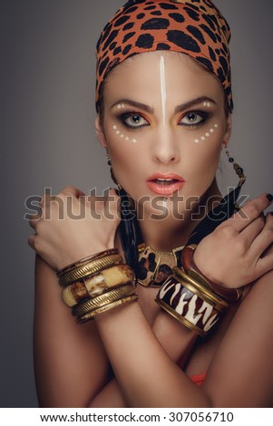 Interesting woman in leopard pattern bandana with art make up posing in studio. Isolated on grey background.
