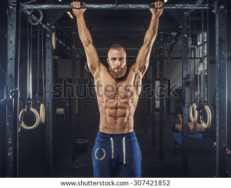 Shirtless muscular man in blue sports pants doing exercises in a gym on horizontal bar.