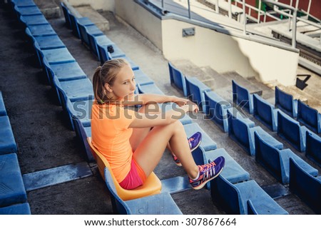 Slim female in sportswear sitting on plastic blue seat on the stadium.