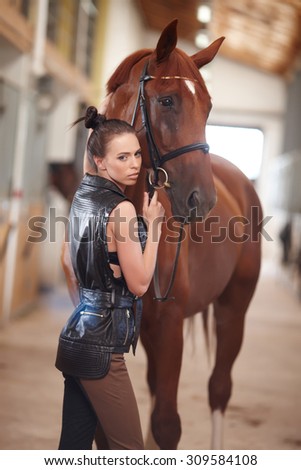 Sexy young woman posing with brown horse in stable.
