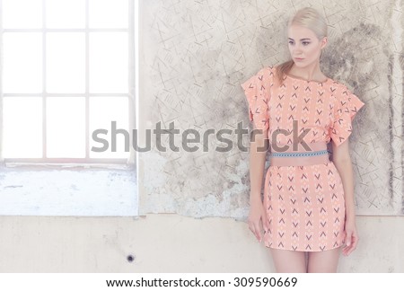 Portrait of blond female in pink dress over grey wall.