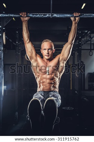 Shirtless muscular man in military pants doing exercises on horizontal bar.