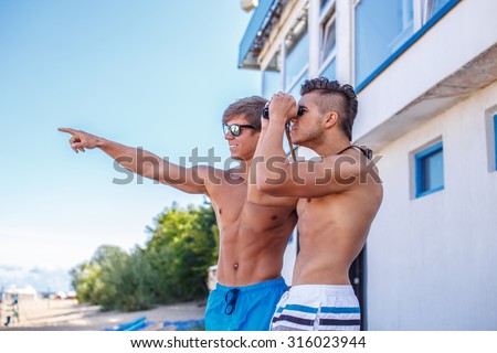 Two awesome muscular guys. One of them looking through binocular, another showing the way with his hand.