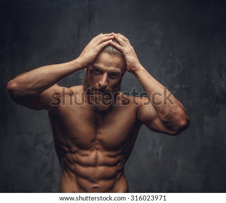 Shirtless muscular guy with beard holding his head with hands.