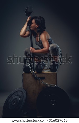 Sporty woman with short black hair sitting on wooden box and holding big black hummer.