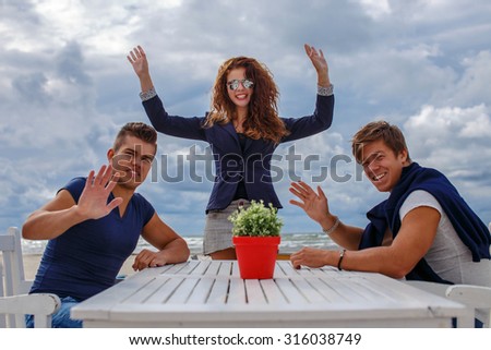 Two mans and one redhead woman at the table on the beach.