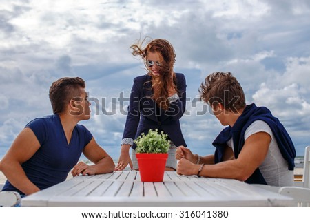 Two mans and one redhead woman at the table on the beach.