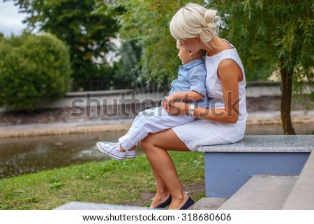 Little boy sitting on his mother knees in a park.