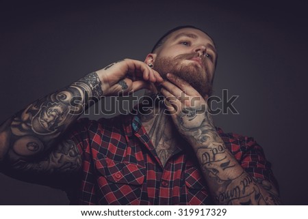 Man in red t shirt and tattooes on hands shaving his beard.