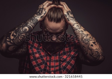 Mans with beard and tattoes on arms holding his head. Isolated on grey background.