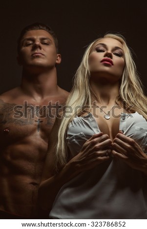 Couple of blond sexy woman and shirtless muscular tattooed man. Isolated on grey background.
