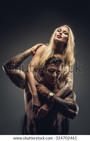 Emotional couple of blond woman in sexy bra and shirtless muscular tattooed man. Isolated on grey background.