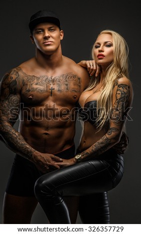 Muscular tattooed man and his blond sexy woman isolated on grey background.