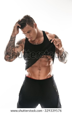Awesome muscular tattooed man putting out his shirt. Isolated on white background.